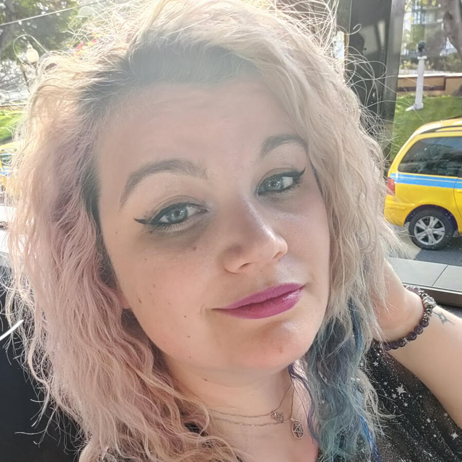 Dr Rosie Fox, taking a selfie at pride. Pink, platinum and blue coloured hair, pink lip and winged eyeliner, sparkly stars on a black dress